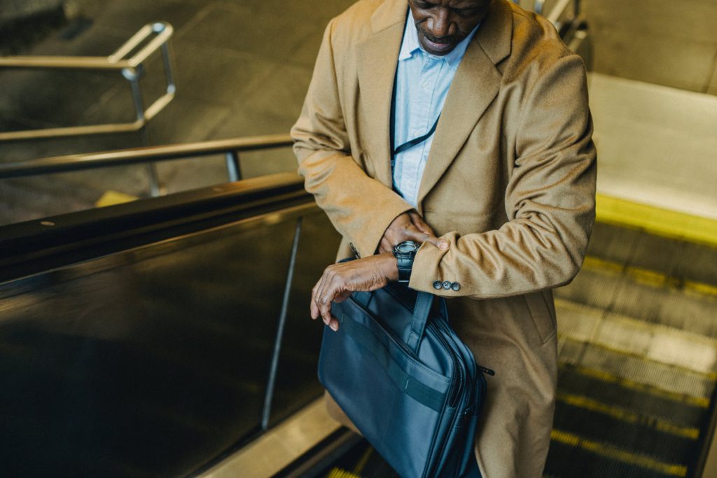 crop black businessman riding escalator and looking at wristwatch