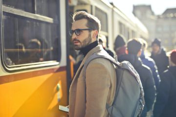man in brown coat and gray backpack posing for a photo