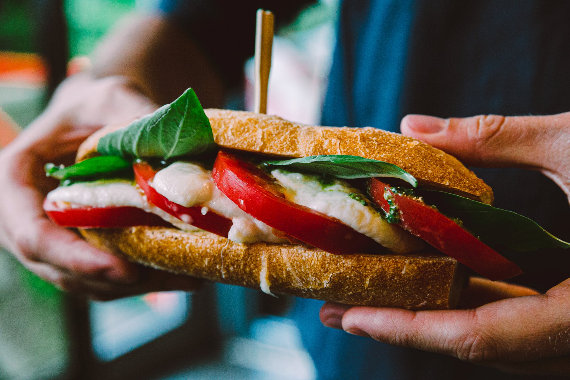 crop unrecognizable man showing delicious sandwich with tomato and cheese